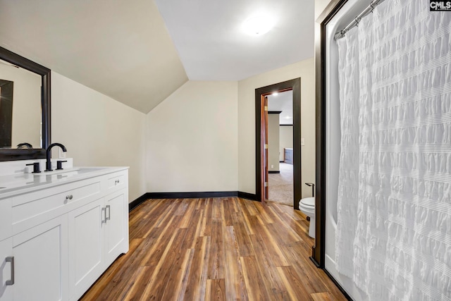 bathroom with hardwood / wood-style flooring, vaulted ceiling, vanity, and toilet