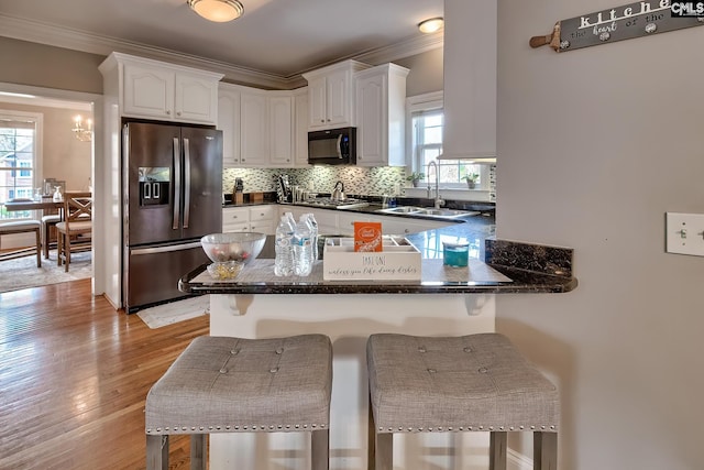 kitchen with a kitchen bar, sink, stainless steel fridge with ice dispenser, kitchen peninsula, and white cabinets