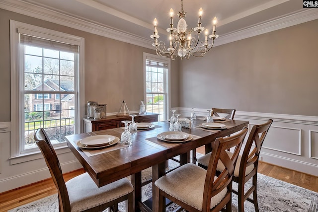 dining area featuring crown molding, a tray ceiling, a chandelier, and light hardwood / wood-style flooring