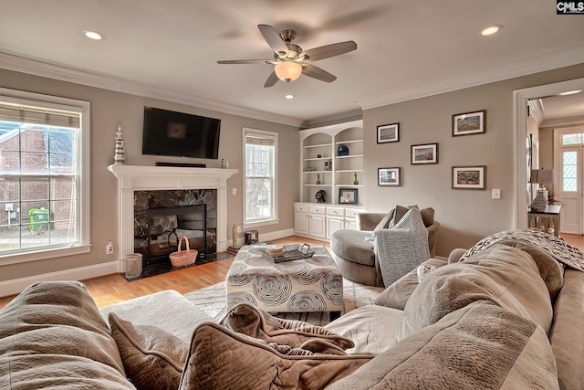 living room featuring light wood-type flooring, ornamental molding, built in features, ceiling fan, and a fireplace