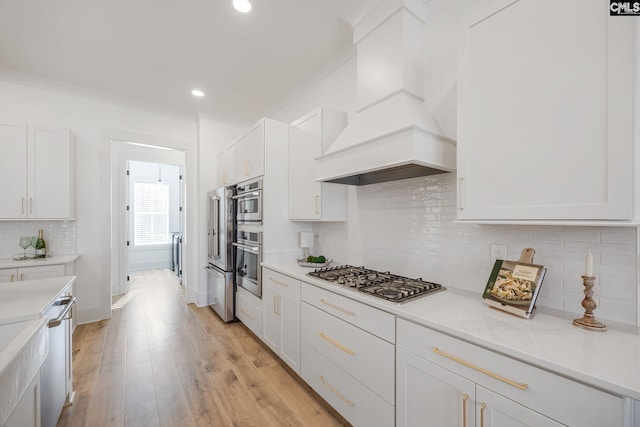 kitchen featuring custom exhaust hood, appliances with stainless steel finishes, white cabinets, and light hardwood / wood-style flooring