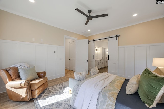 bedroom with ceiling fan, ornamental molding, a barn door, and light hardwood / wood-style floors