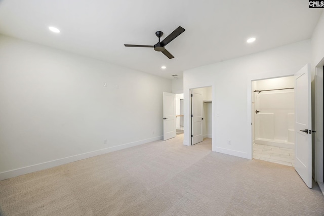 unfurnished bedroom featuring light carpet, ensuite bath, a walk in closet, and ceiling fan