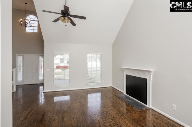 unfurnished living room featuring ceiling fan with notable chandelier, dark wood-type flooring, high vaulted ceiling, and a healthy amount of sunlight