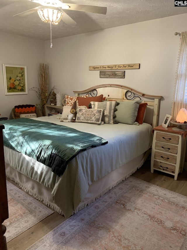 bedroom with ceiling fan, hardwood / wood-style floors, and a textured ceiling