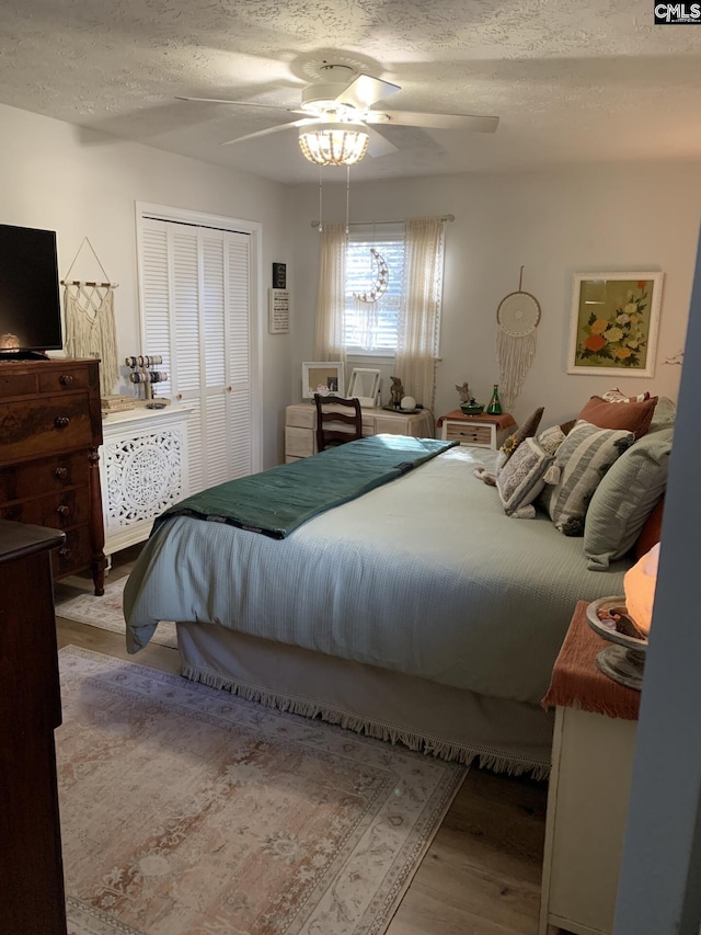 bedroom with ceiling fan, a closet, light hardwood / wood-style flooring, and a textured ceiling