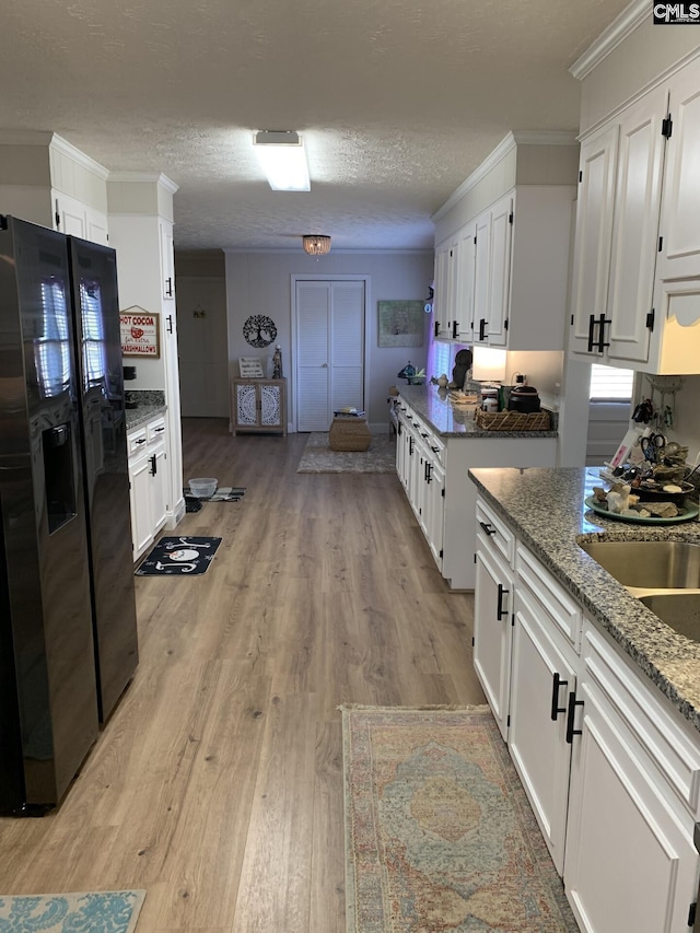 kitchen with white cabinetry, ornamental molding, stone countertops, stainless steel fridge with ice dispenser, and light wood-type flooring