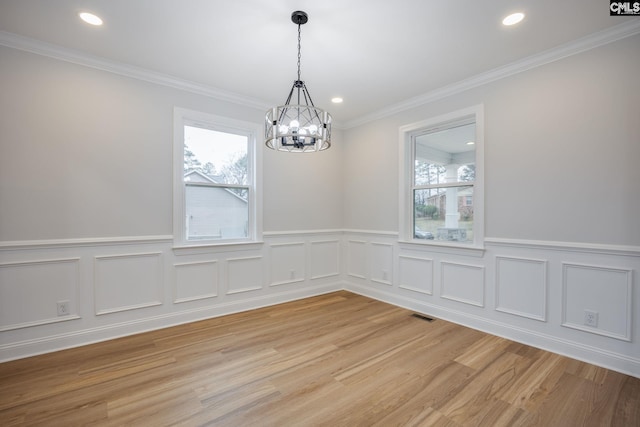 unfurnished dining area with crown molding, a wealth of natural light, a chandelier, and wood-type flooring