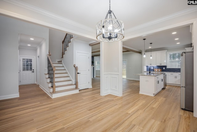 kitchen with sink, white cabinets, stainless steel fridge, hanging light fixtures, and a center island with sink