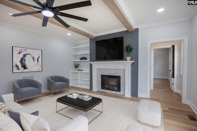 living room featuring light hardwood / wood-style flooring, beam ceiling, ornamental molding, a brick fireplace, and built in shelves