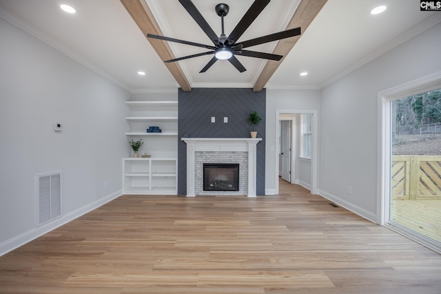 unfurnished living room with crown molding, ceiling fan, beam ceiling, a tiled fireplace, and light hardwood / wood-style floors