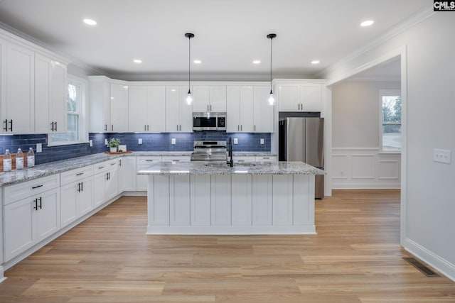 kitchen featuring sink, appliances with stainless steel finishes, white cabinetry, an island with sink, and decorative light fixtures