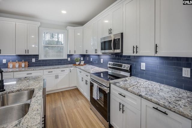 kitchen with white cabinetry, stainless steel appliances, light hardwood / wood-style flooring, and backsplash