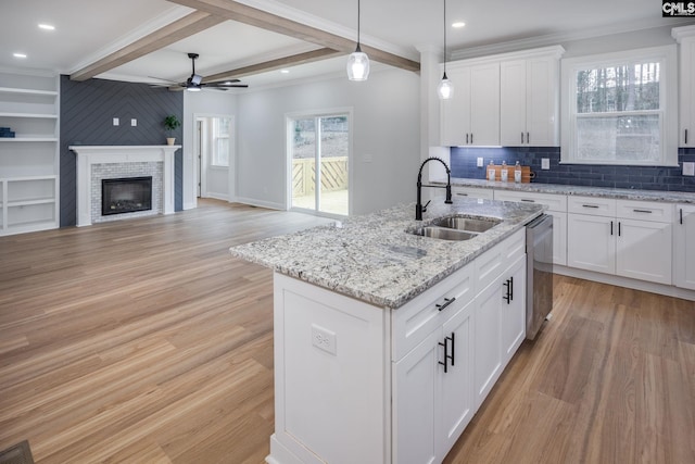 kitchen featuring sink, white cabinetry, decorative light fixtures, stainless steel dishwasher, and a kitchen island with sink