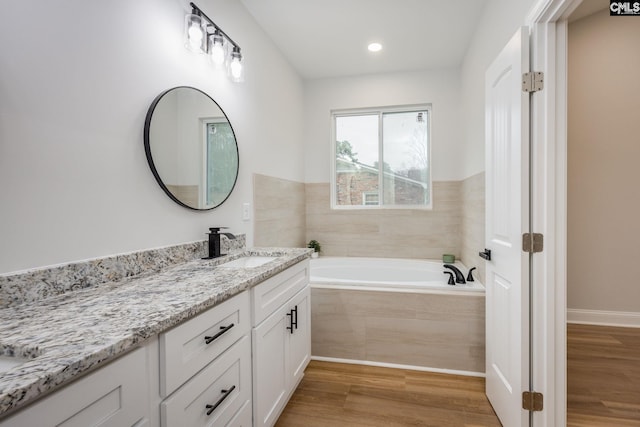 bathroom featuring wood-type flooring, tiled bath, and vanity