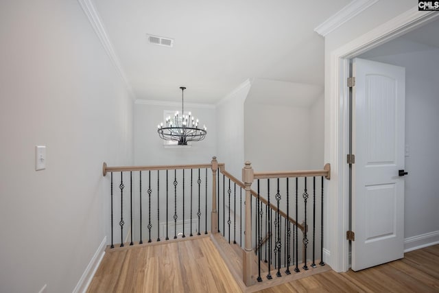 stairway with wood-type flooring, ornamental molding, and an inviting chandelier