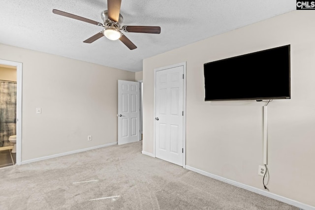 unfurnished bedroom featuring light carpet, ceiling fan, ensuite bath, and a textured ceiling