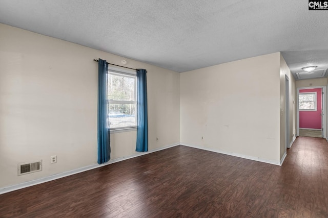 empty room featuring plenty of natural light, a textured ceiling, and dark hardwood / wood-style flooring