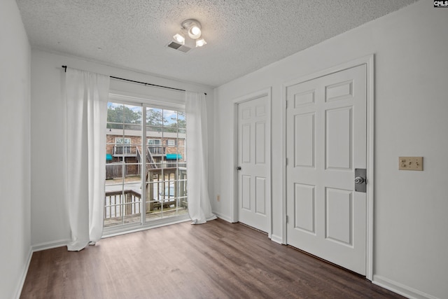 unfurnished bedroom featuring access to outside, dark hardwood / wood-style floors, and a textured ceiling