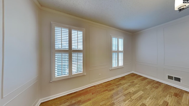 spare room featuring ornamental molding, plenty of natural light, light hardwood / wood-style floors, and a textured ceiling