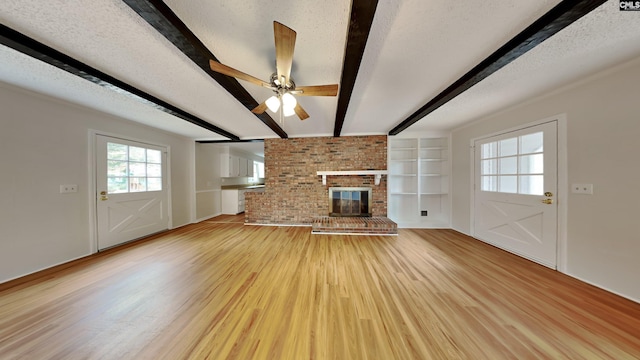 unfurnished living room featuring ceiling fan, a fireplace, a textured ceiling, beamed ceiling, and light wood-type flooring