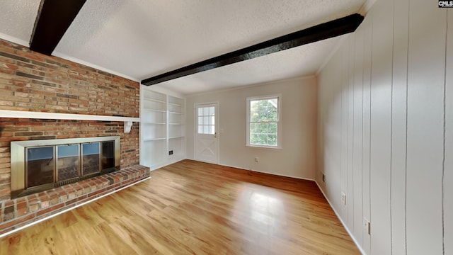 unfurnished living room featuring light hardwood / wood-style flooring, built in features, a textured ceiling, a brick fireplace, and beamed ceiling