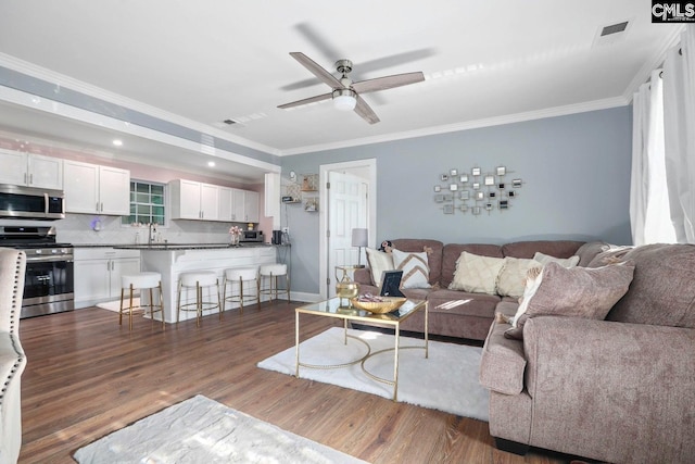 living room featuring dark wood-type flooring, ceiling fan, ornamental molding, and sink