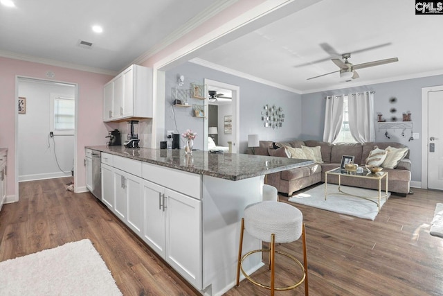 kitchen featuring a breakfast bar area, white cabinetry, dark stone countertops, dishwasher, and a healthy amount of sunlight