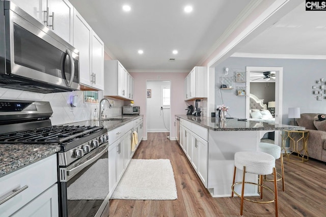 kitchen with sink, a breakfast bar, appliances with stainless steel finishes, white cabinetry, and dark stone counters