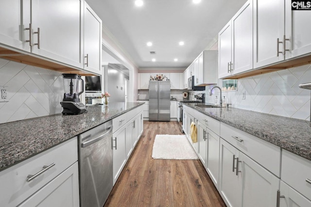 kitchen featuring appliances with stainless steel finishes, white cabinetry, sink, dark stone countertops, and hardwood / wood-style flooring