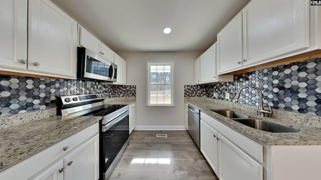 kitchen with light stone counters, sink, white cabinets, and appliances with stainless steel finishes