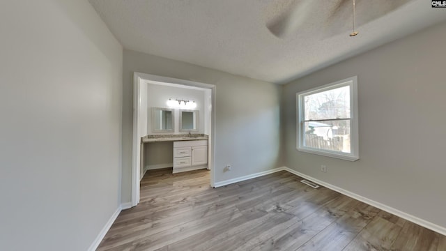 unfurnished bedroom featuring ensuite bathroom, sink, light hardwood / wood-style flooring, and a textured ceiling