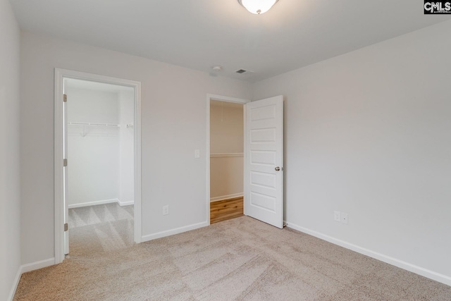 unfurnished bedroom with a closet, carpet, a walk in closet, and baseboards