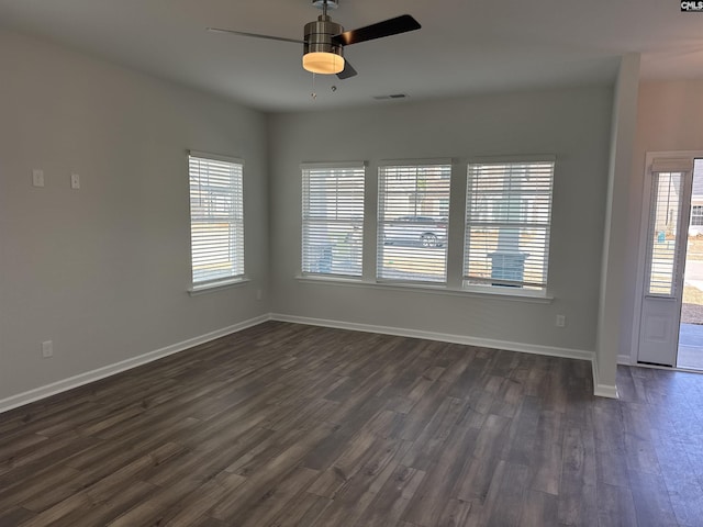 empty room with visible vents, dark wood-style flooring, a ceiling fan, and baseboards