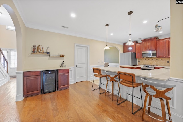 kitchen with decorative light fixtures, light hardwood / wood-style flooring, ornamental molding, appliances with stainless steel finishes, and beverage cooler