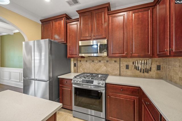 kitchen featuring backsplash, light tile patterned floors, ornamental molding, and stainless steel appliances