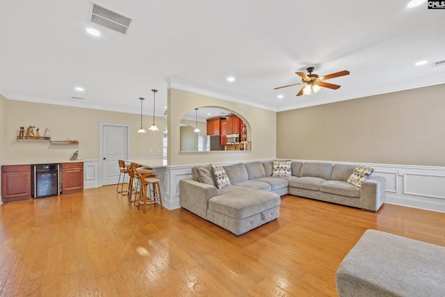 living room with wine cooler, light hardwood / wood-style flooring, ornamental molding, and bar area