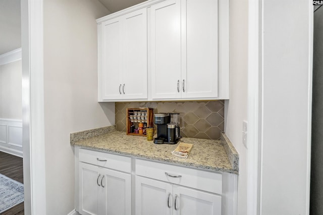 bar featuring light stone countertops, white cabinets, and backsplash