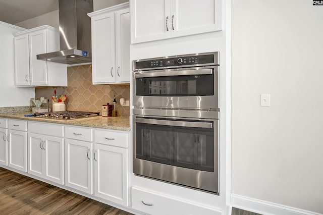 kitchen featuring appliances with stainless steel finishes, tasteful backsplash, white cabinetry, light stone countertops, and wall chimney exhaust hood