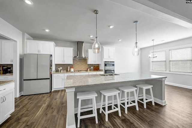 kitchen with stainless steel appliances, an island with sink, white cabinets, and wall chimney exhaust hood