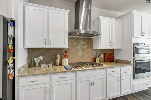 kitchen with white cabinets, appliances with stainless steel finishes, decorative backsplash, and wall chimney range hood