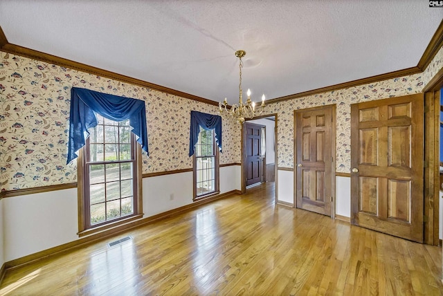 unfurnished dining area with an inviting chandelier, crown molding, a textured ceiling, and light wood-type flooring