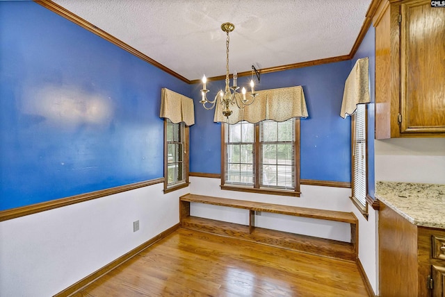 unfurnished dining area with ornamental molding, a chandelier, light hardwood / wood-style flooring, and a textured ceiling