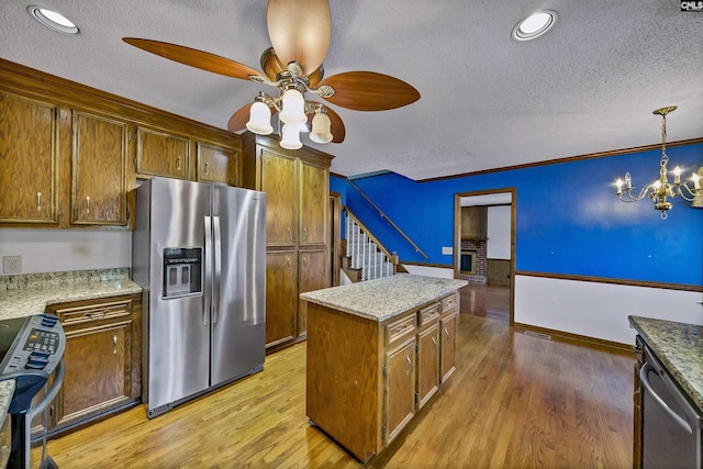 kitchen with appliances with stainless steel finishes, pendant lighting, light wood-type flooring, a center island, and a textured ceiling