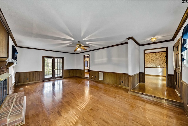 unfurnished living room featuring wood walls, hardwood / wood-style flooring, a brick fireplace, a textured ceiling, and french doors