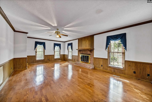 unfurnished living room with wood walls, a textured ceiling, a fireplace, and light hardwood / wood-style floors