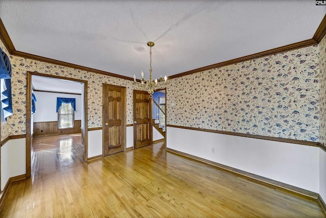 unfurnished dining area with ornamental molding, a chandelier, a textured ceiling, and light hardwood / wood-style floors