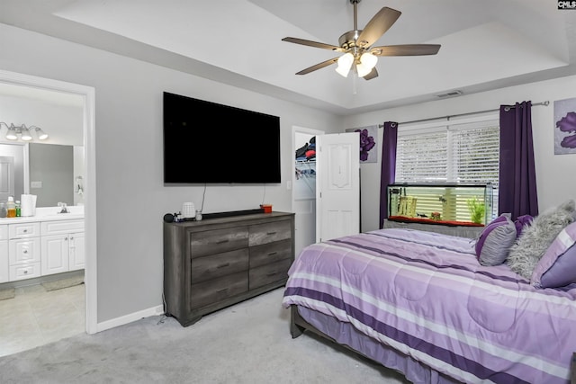 carpeted bedroom featuring sink, ceiling fan, ensuite bathroom, a walk in closet, and a raised ceiling