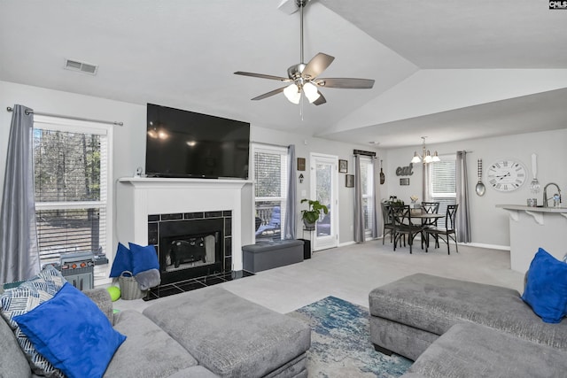 carpeted living room featuring ceiling fan with notable chandelier, vaulted ceiling, and a tile fireplace