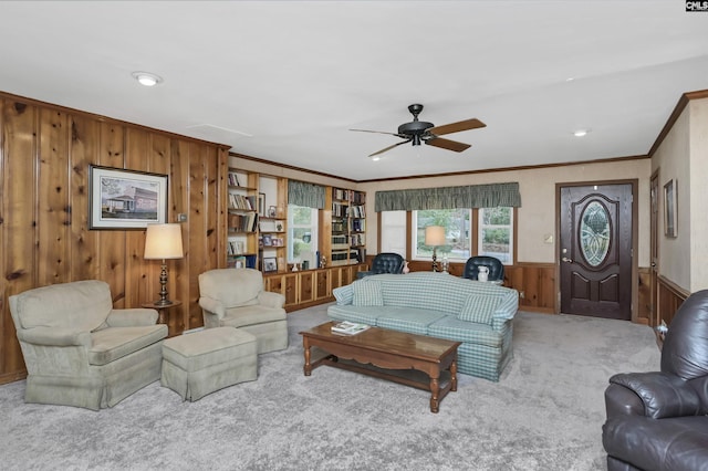 carpeted living room featuring crown molding, wooden walls, and ceiling fan